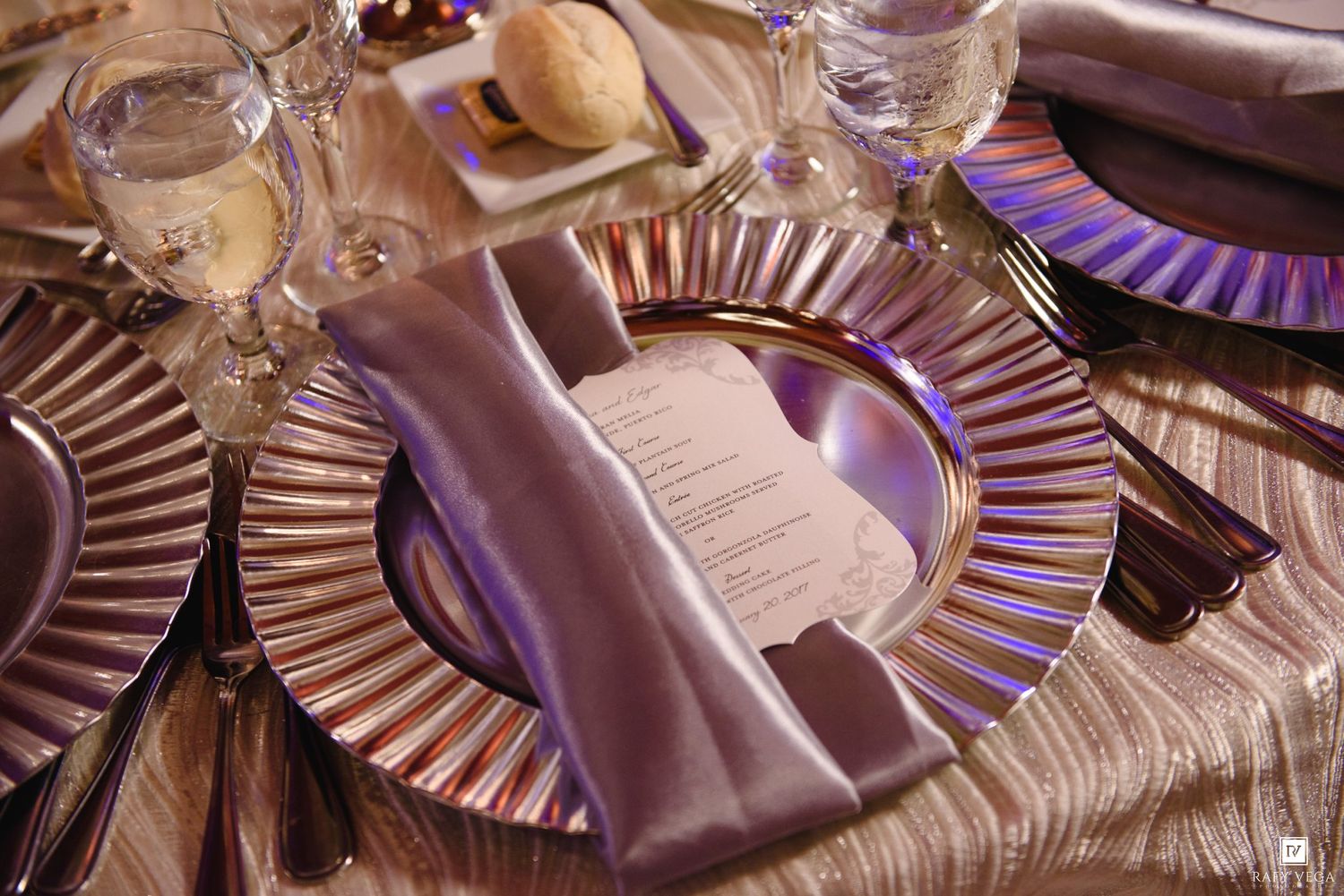 Luxurious place setting with purple charger plate, folded napkin, and printed menu card on textured tablecloth.