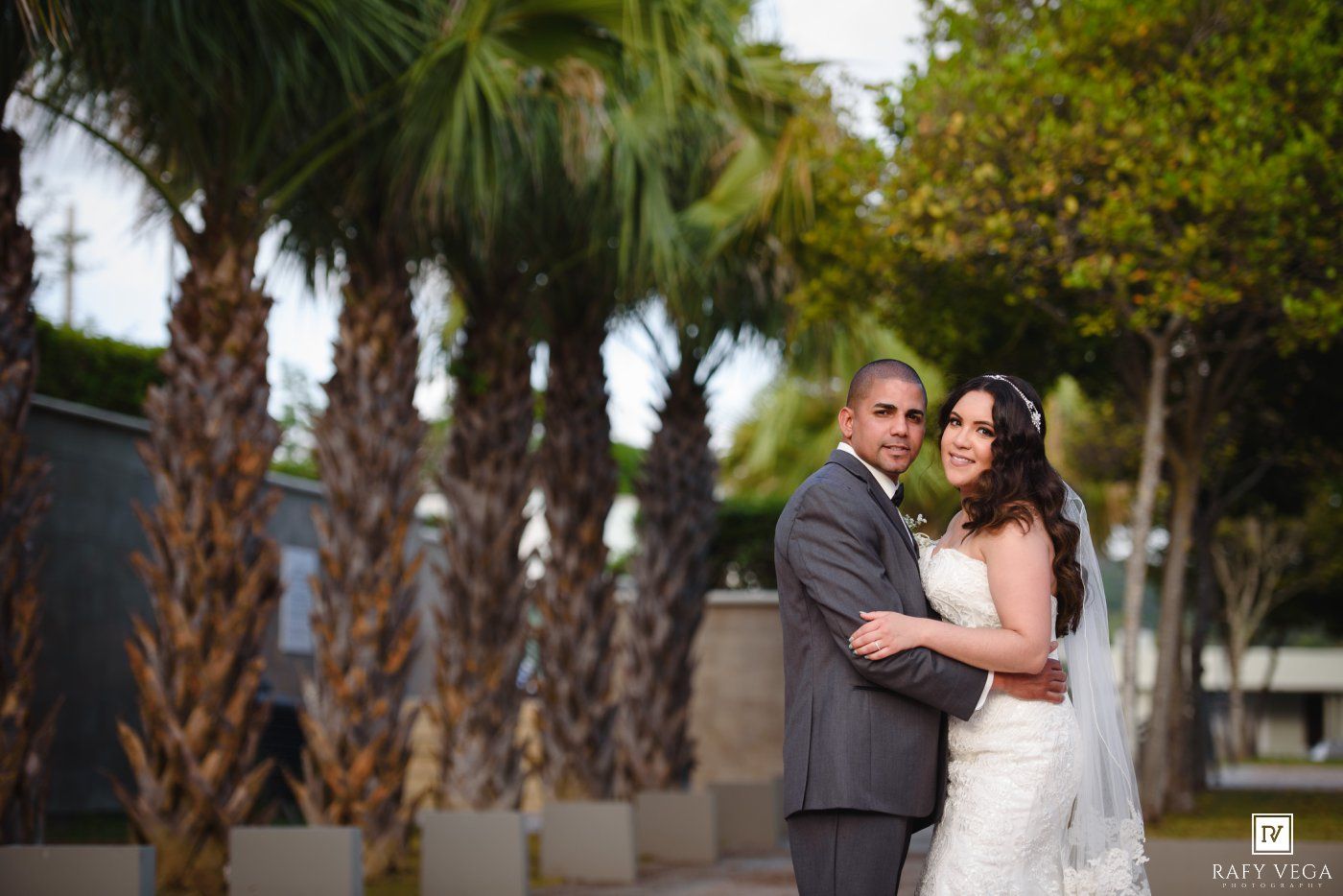 Elegant bride and groom posing together outdoors surrounded by lush palm trees on their wedding day.