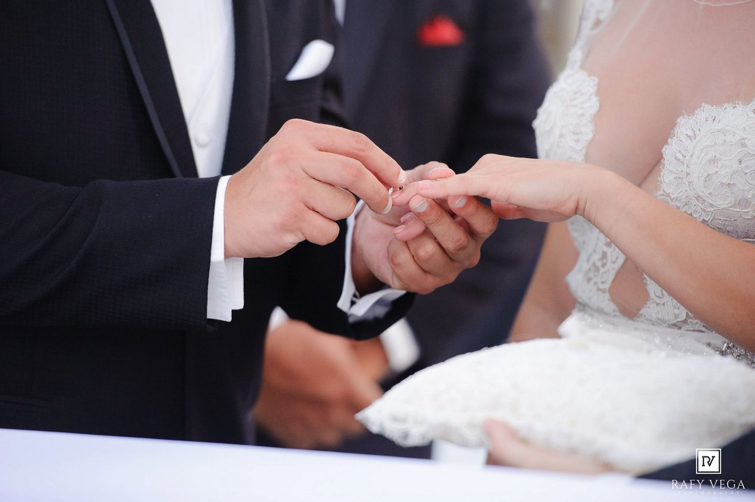 Groom placing wedding ring on bride's finger during outdoor ceremony, close-up of hands in elegant wedding attire.