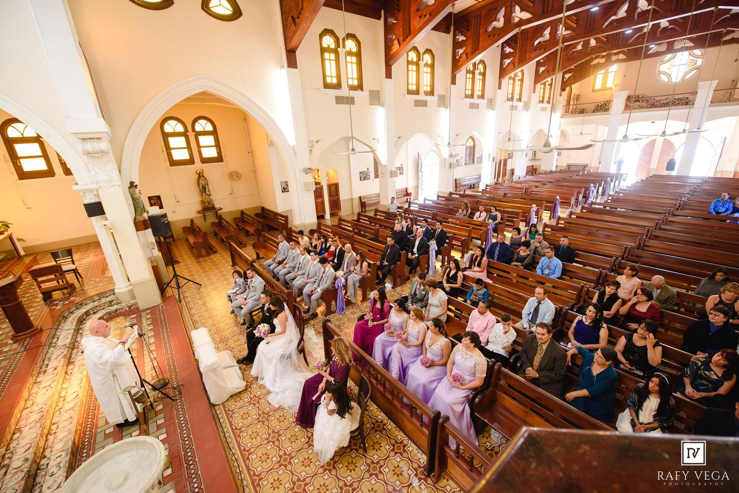 Aerial view of a wedding ceremony inside a beautiful church with guests seated in wooden pews.
