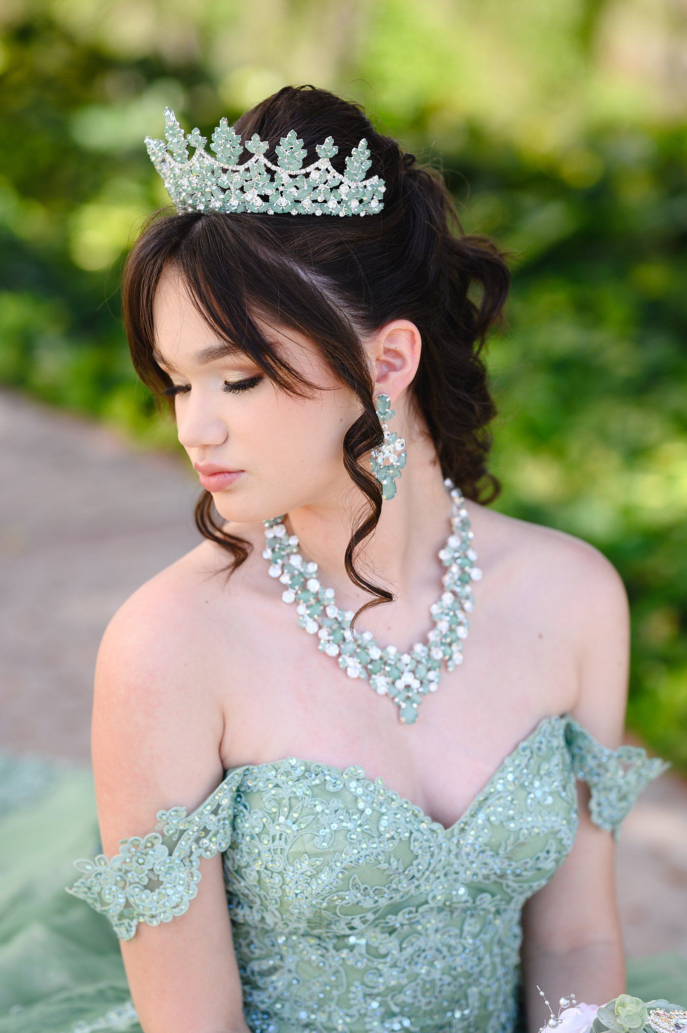Young woman in mint green off-shoulder gown wearing crystal tiara and matching jewelry set for quinceañera.
