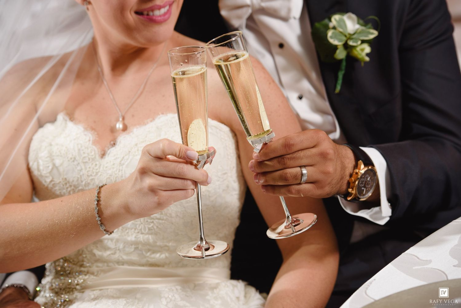Bride and groom clinking champagne flutes during wedding reception toast, bride in white lace gown.