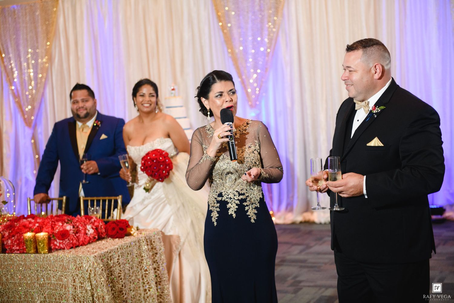 Wedding reception toast with bride holding microphone, groom in tuxedo, and guests celebrating in elegant ballroom.