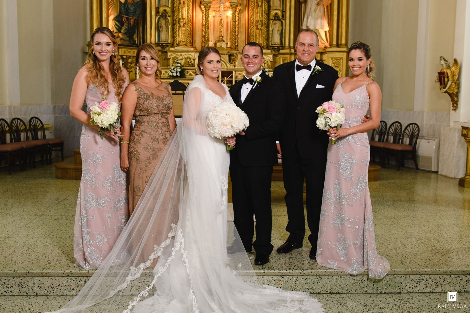A bride and groom pose with bridesmaids and groomsmen inside an ornate church after their wedding ceremony.