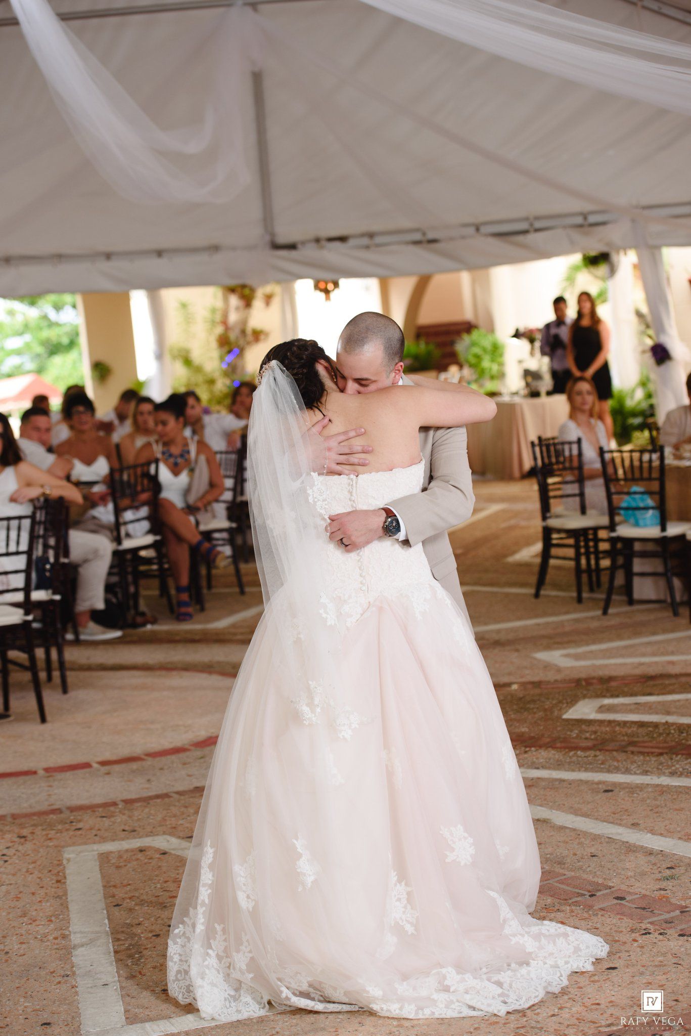 Bride and groom share their first dance under a white draped tent at an outdoor wedding reception.