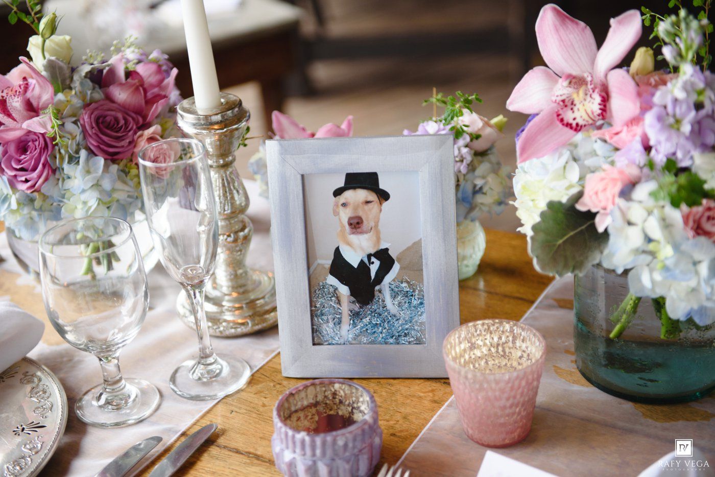 Framed illustration of a dressed dog serves as a whimsical wedding table centerpiece with pink flowers.
