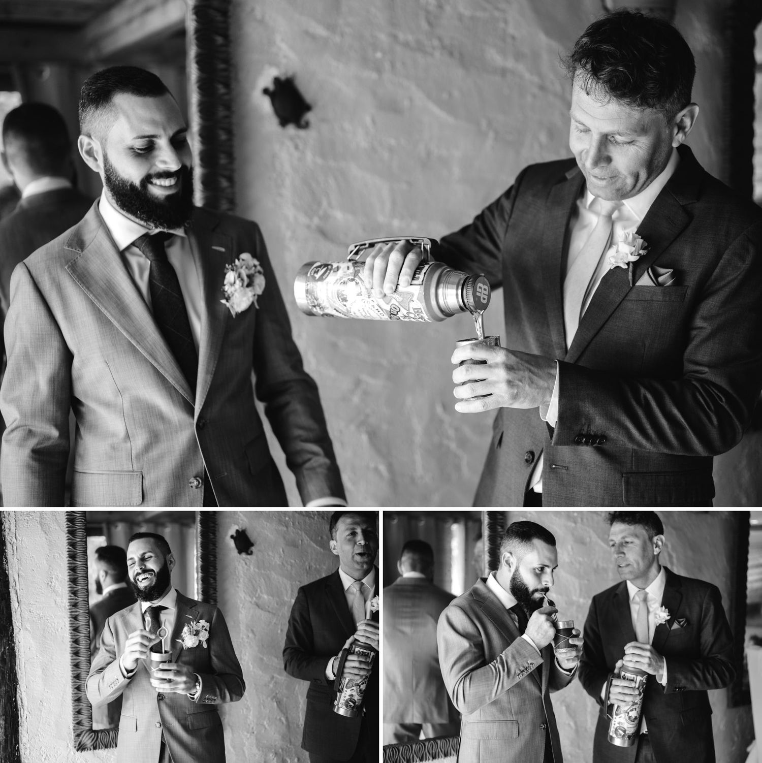 Black and white wedding photo of two groomsmen in suits sharing a drink and laughing together.