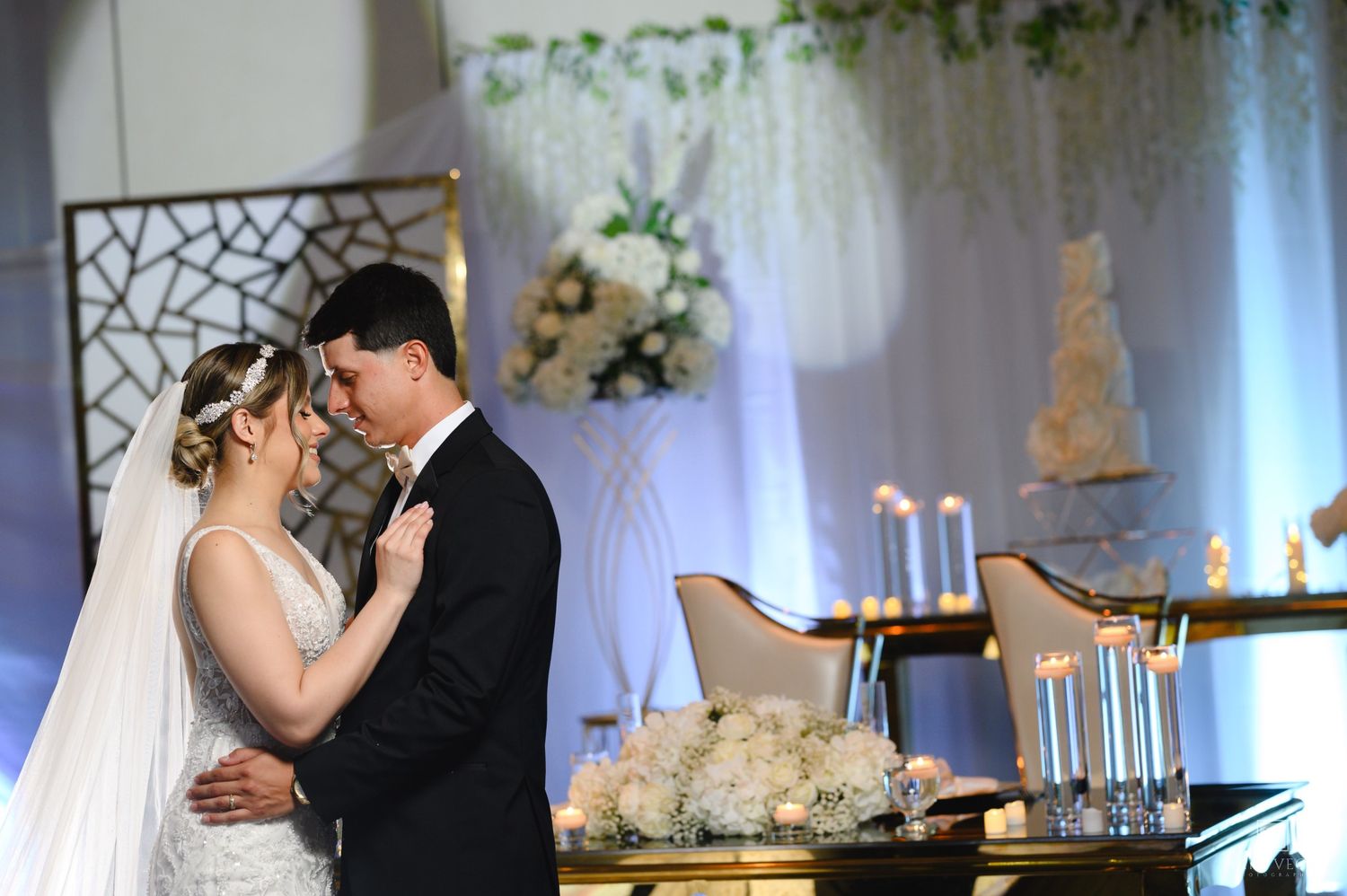 Newlyweds share a romantic first dance surrounded by white floral arrangements and candlelight at their wedding reception.