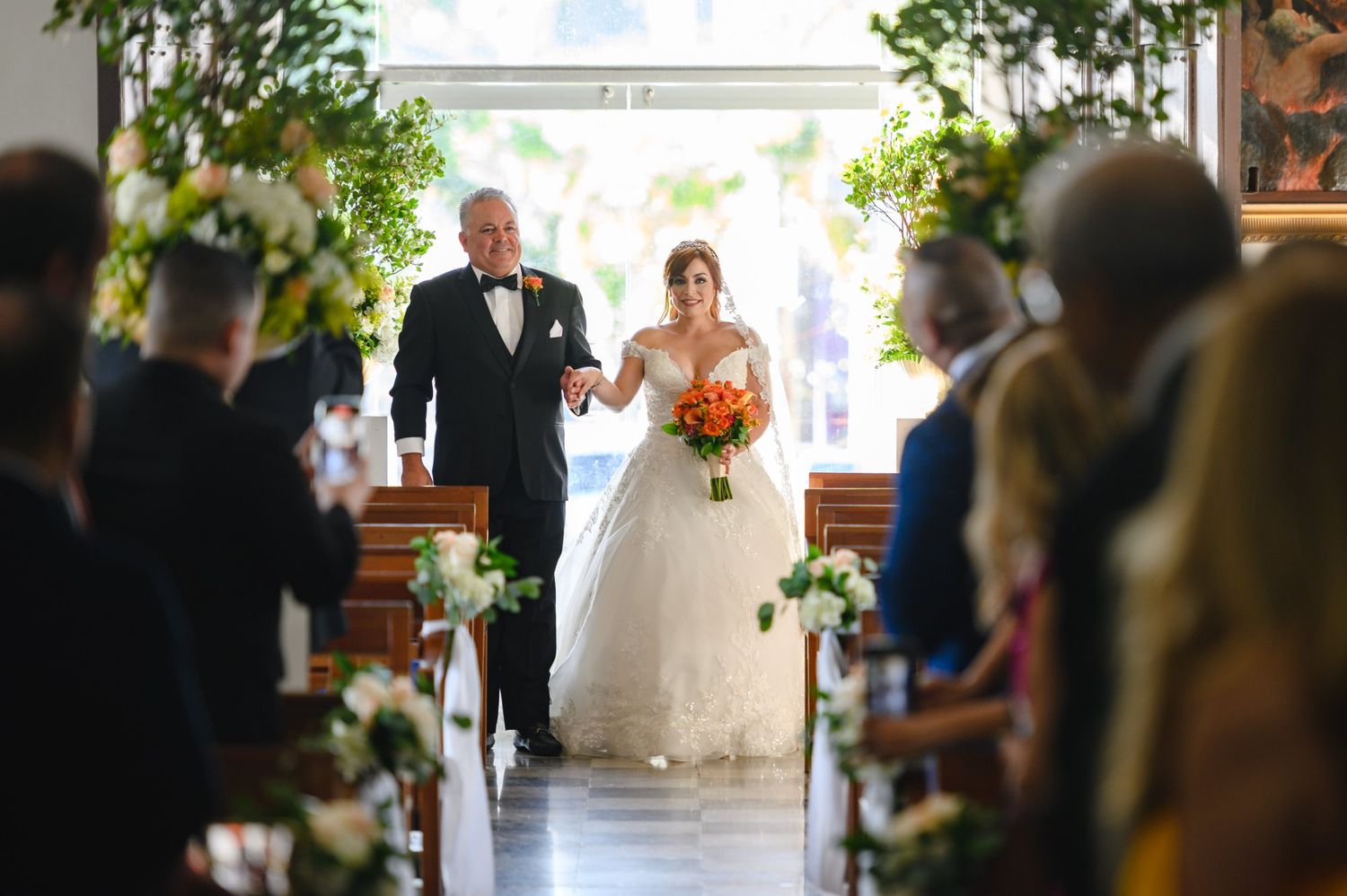 Bride walks down the aisle with escort at elegant church wedding ceremony with floral arrangements.