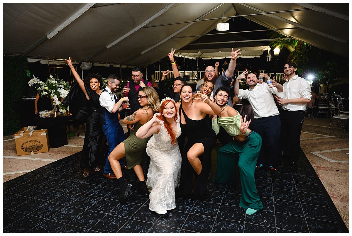Wedding party and guests strike fun poses together on the dance floor at a tented outdoor reception.