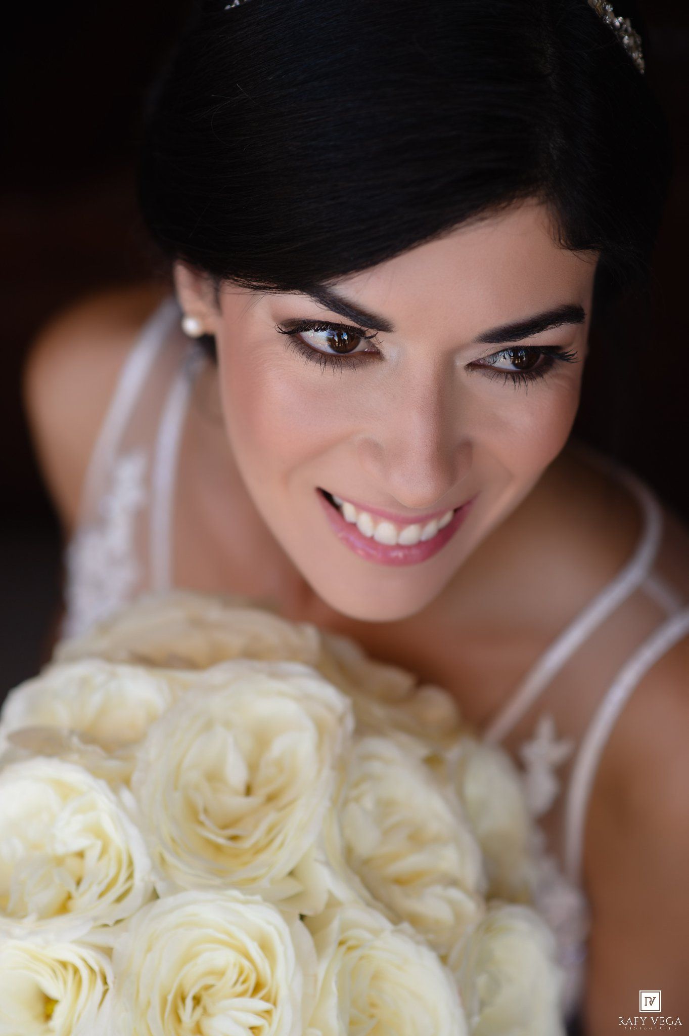 Smiling bride with dark hair holding a bouquet of white roses on her wedding day.
