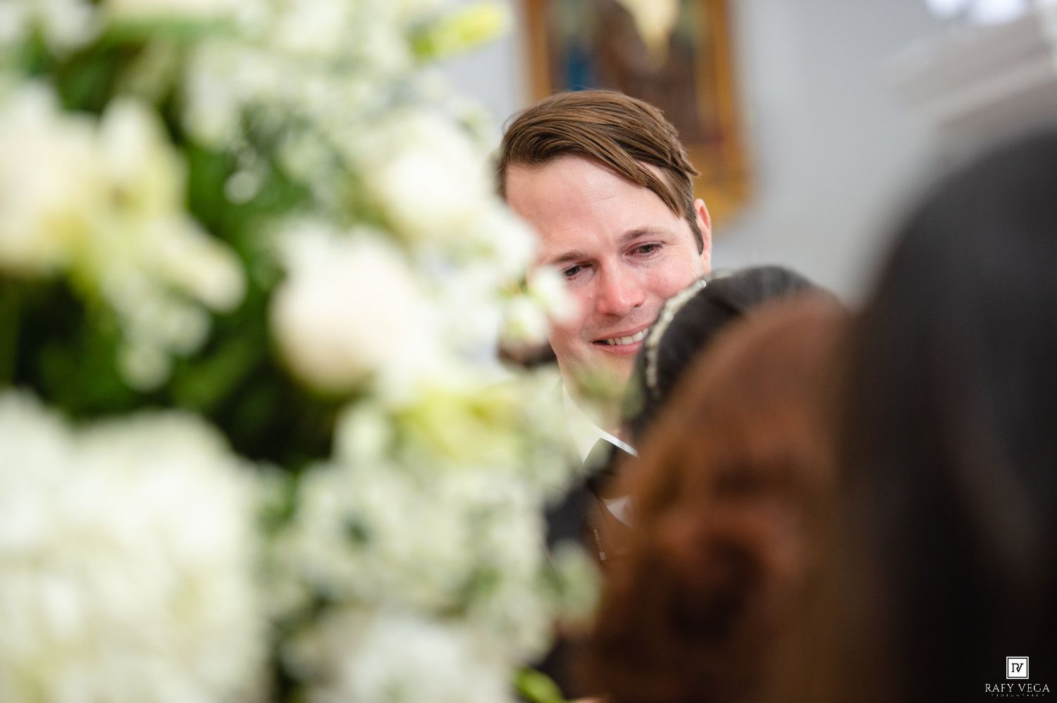Man smiling among white floral arrangements at a wedding ceremony.