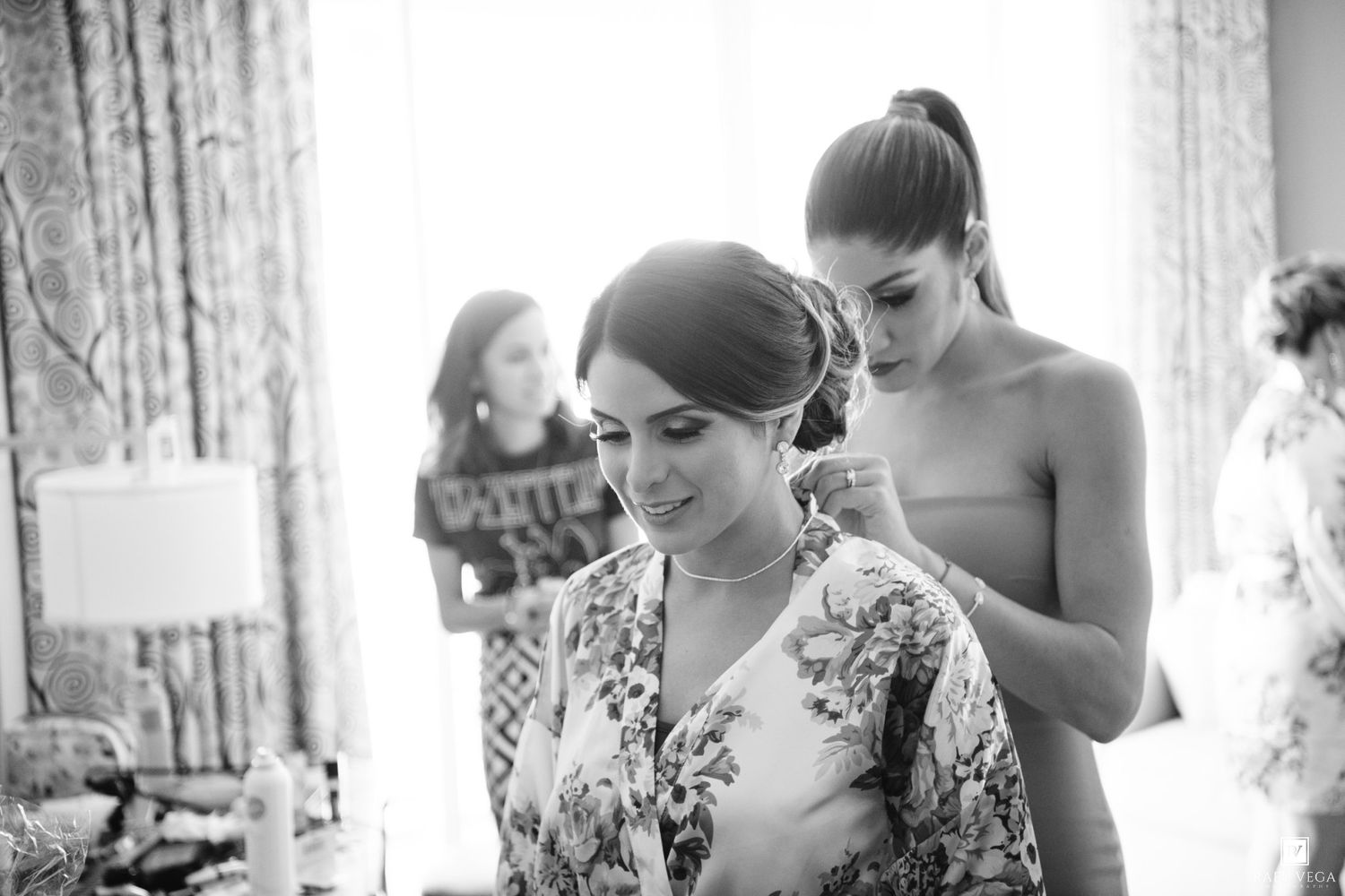 Bridesmaid helping bride with floral robe during wedding preparations in elegant black and white photo.