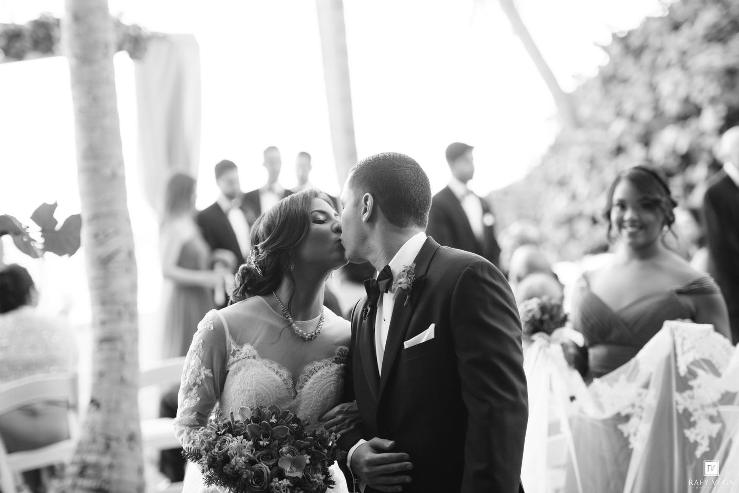 Black and white photo of a bride and groom sharing their first kiss at an outdoor wedding ceremony.