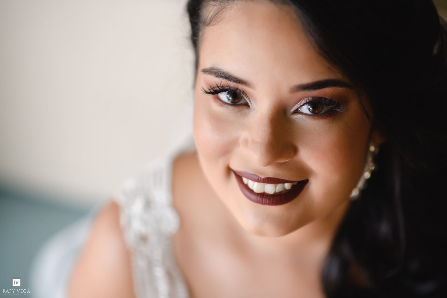 Close-up portrait of a smiling bride in white lace dress with elegant makeup and pearl earrings on her wedding day.