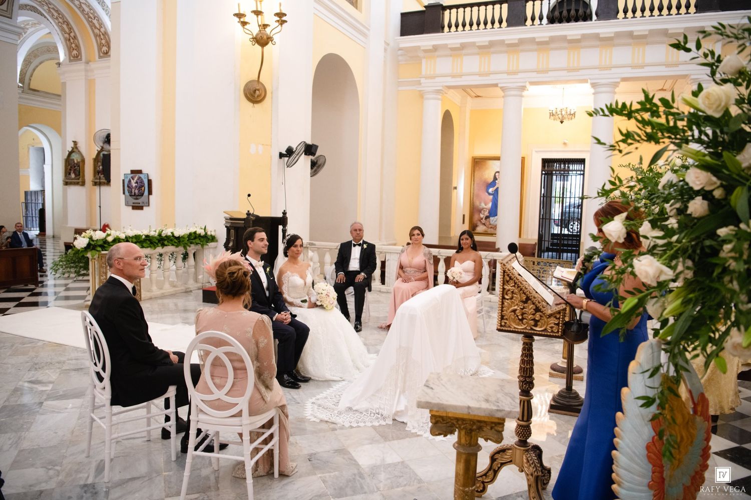 Elegant wedding ceremony in ornate church with seated guests and officiant reading vows.