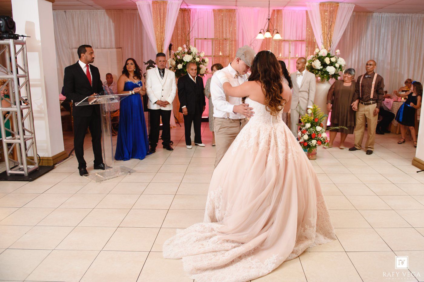 Bride and groom share their first dance at elegant wedding reception with guests watching and floral decorations.