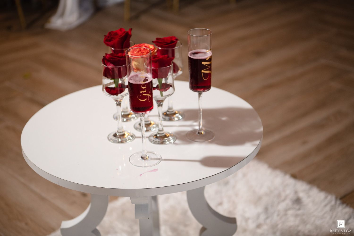 Elegant white round table with red rose centerpiece and crystal champagne glasses filled with red wine.