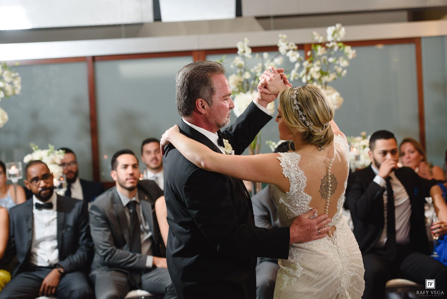 Bride and groom share first dance at elegant wedding reception with seated guests watching in background.