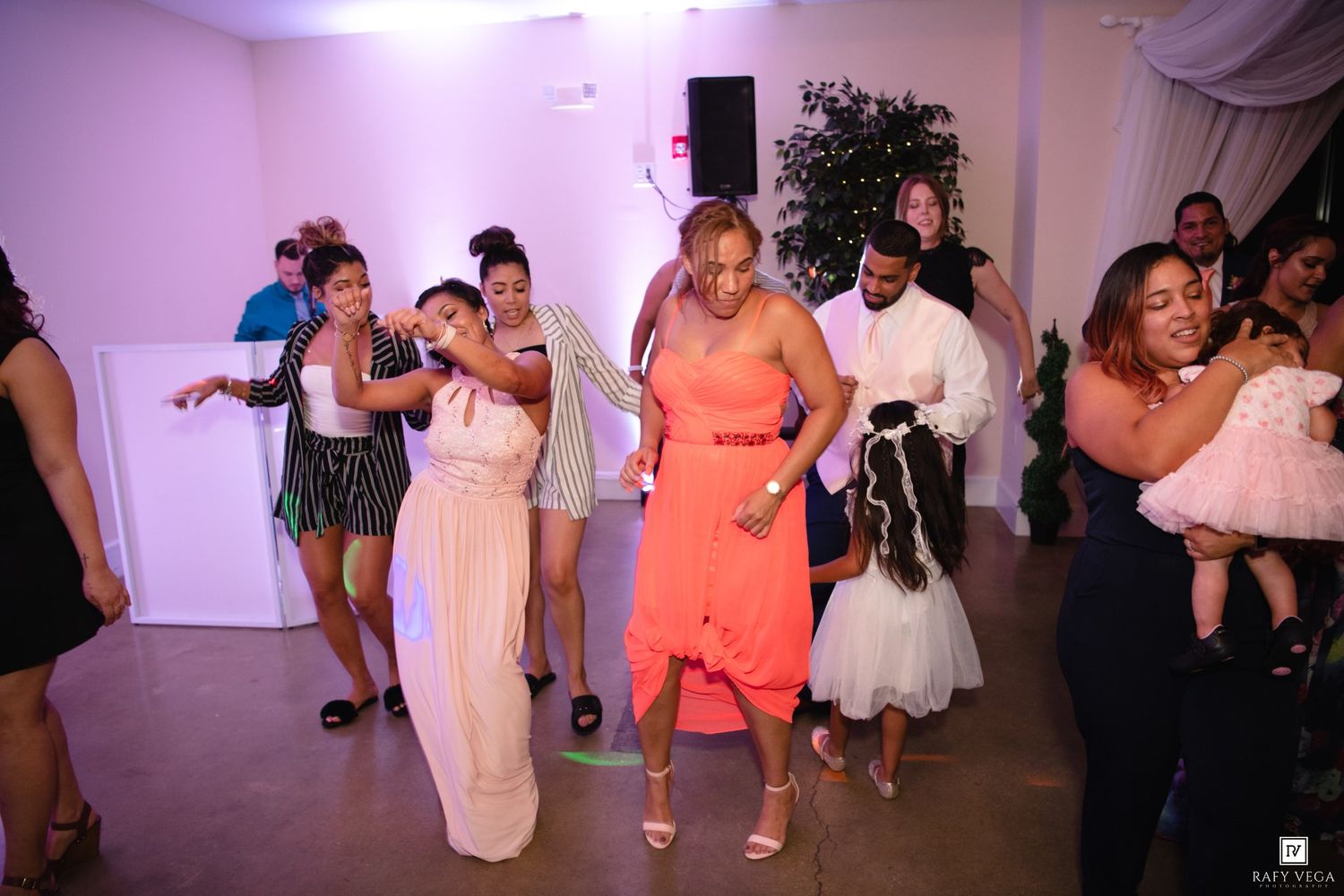 Guests in colorful formal attire dancing energetically at a lively wedding reception party.