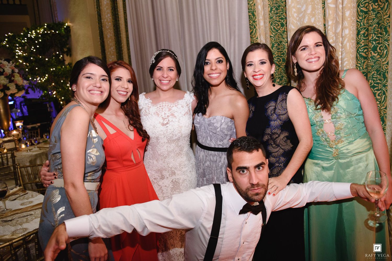 Group of six women and one man posing together at an elegant wedding reception venue.
