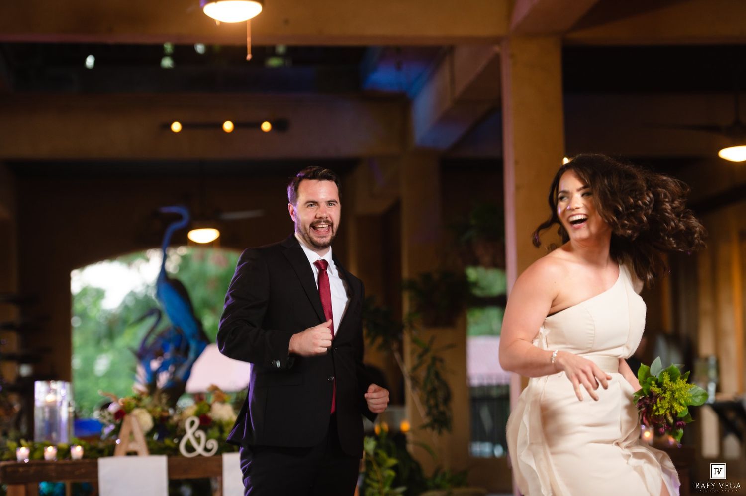 Joyful bride and groom making grand entrance at elegant wedding reception with peacock decor and string lights.