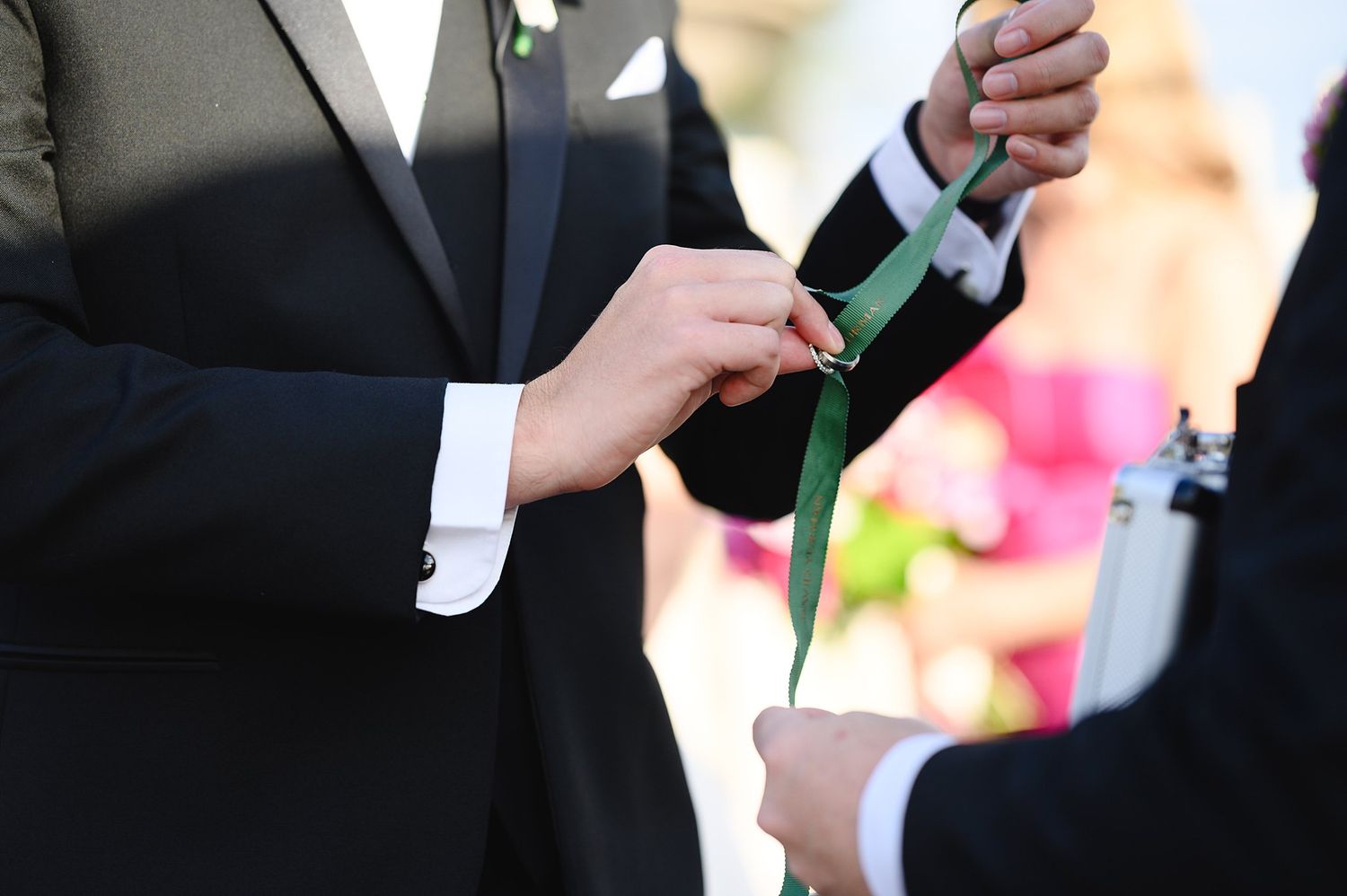 Groom placing a green ribbon ring during an outdoor wedding ceremony.