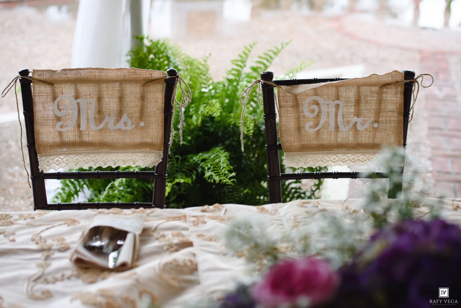 Mr. and Mrs. burlap wedding chair signs decorated with ferns and purple flowers at reception.