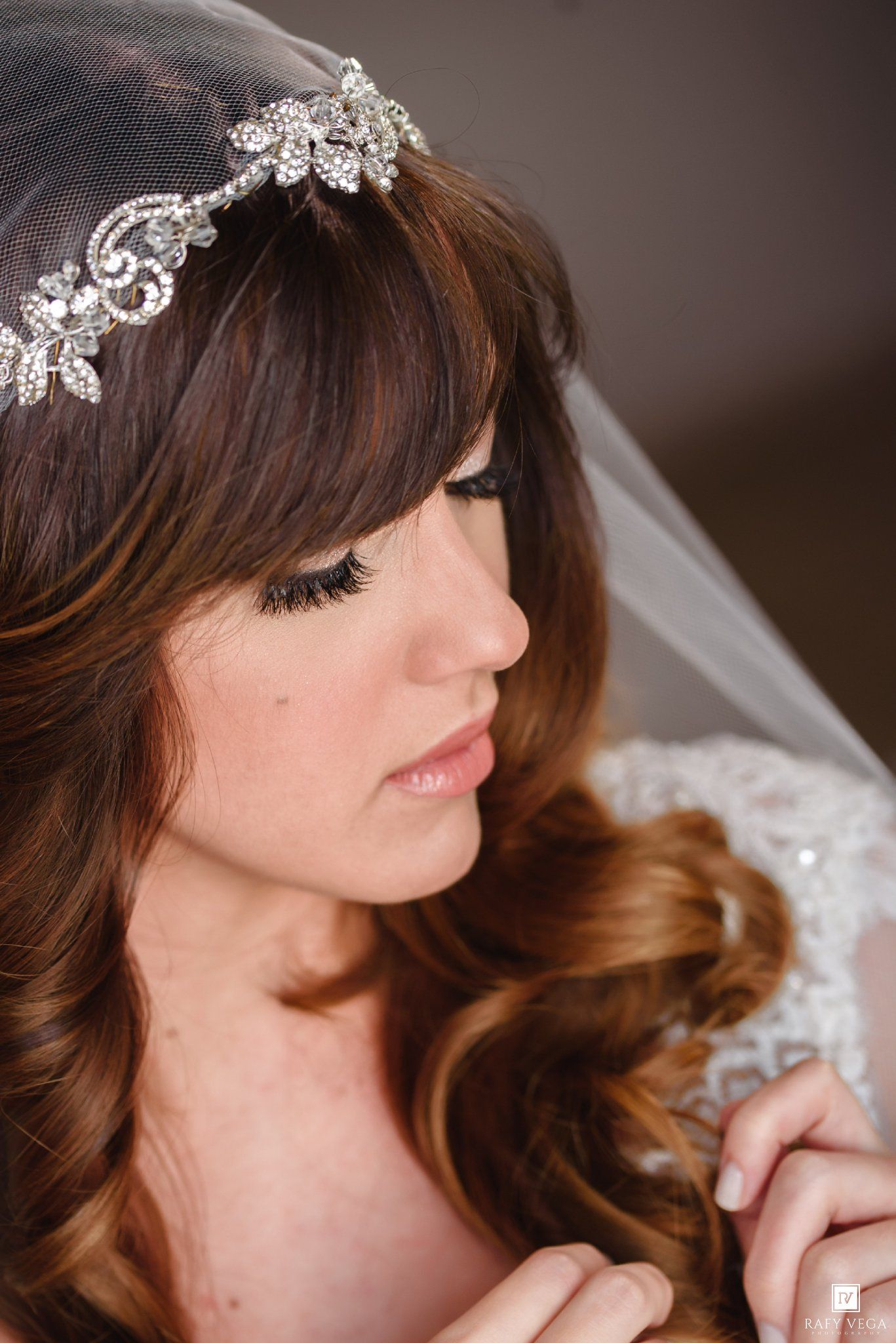 Bride wearing a crystal rhinestone headpiece with a veil over auburn curly hair and lace wedding dress.