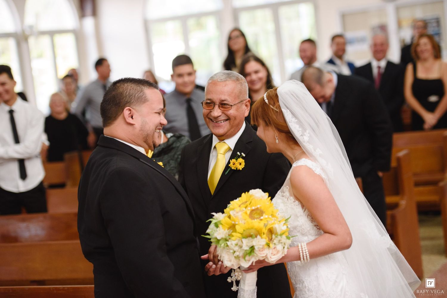 Smiling groom meets bride at church altar as officiant in yellow tie presides over wedding ceremony.