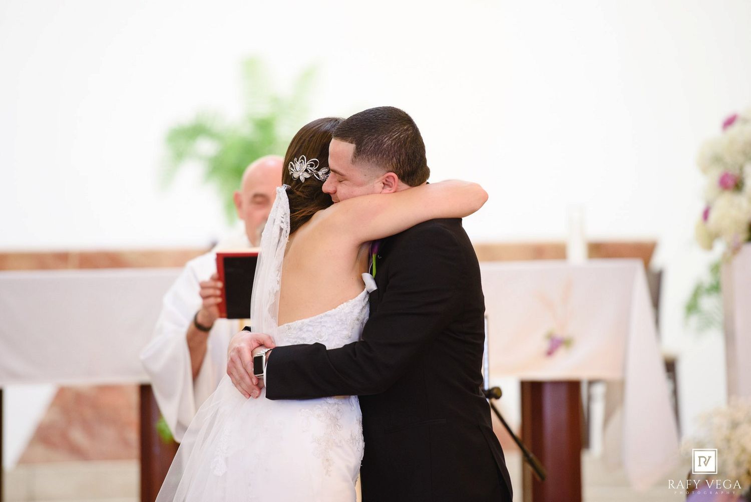 Bride and groom share a heartfelt hug at the altar during their wedding ceremony in a white church.