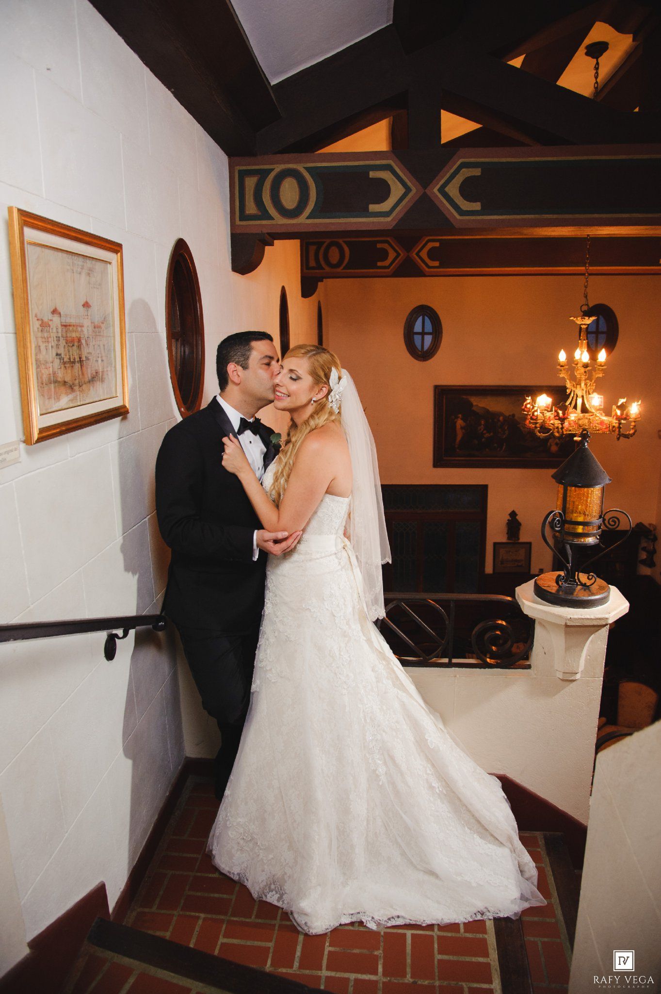 Bride and groom sharing a romantic kiss in a warmly lit Spanish-style venue interior.