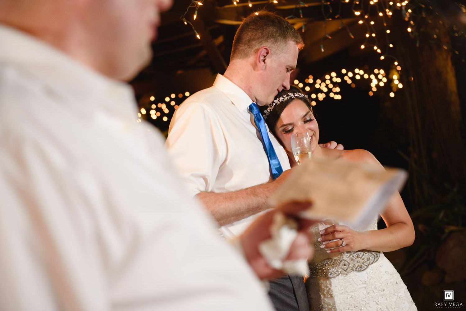Emotional bride and groom exchanging wedding vows indoors with warm fairy lights glowing in the background.