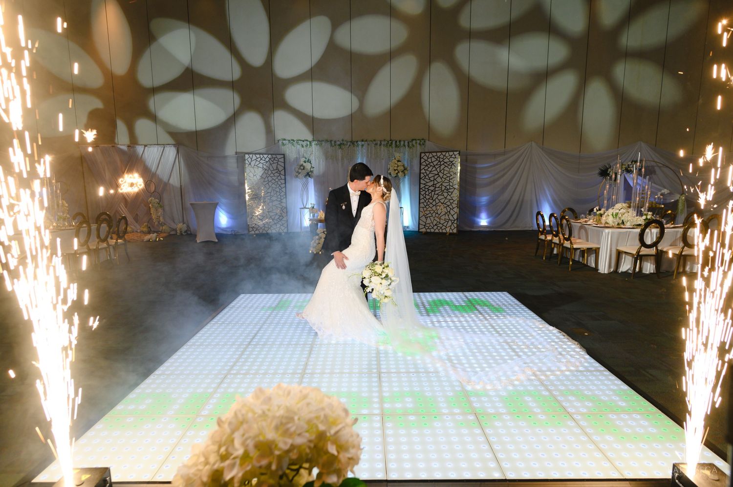 Bride and groom share first dance on illuminated floor with sparkling fireworks at elegant wedding reception.