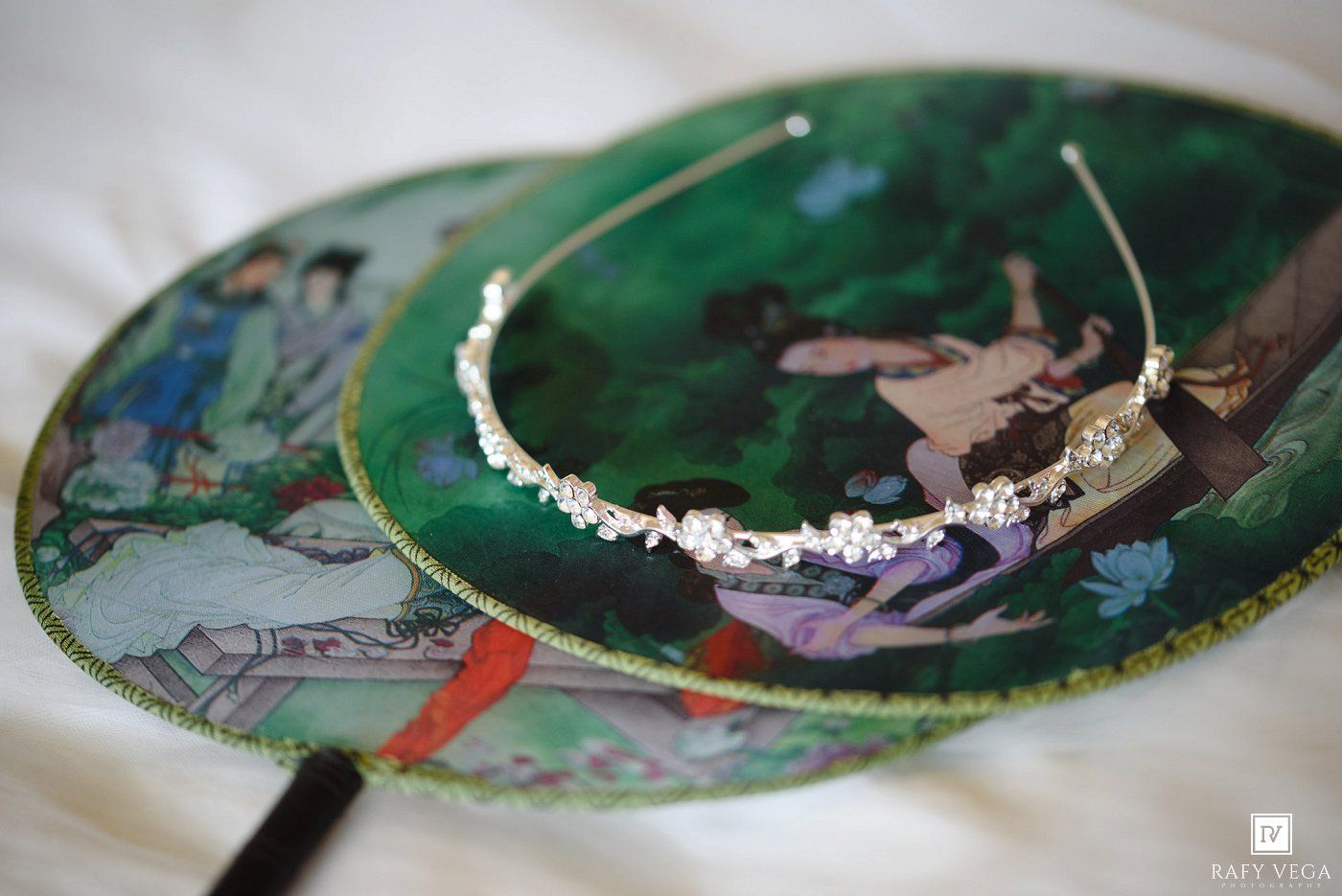 Elegant crystal bridal tiara displayed on a decorative Asian-painted fan with green and gold accents.