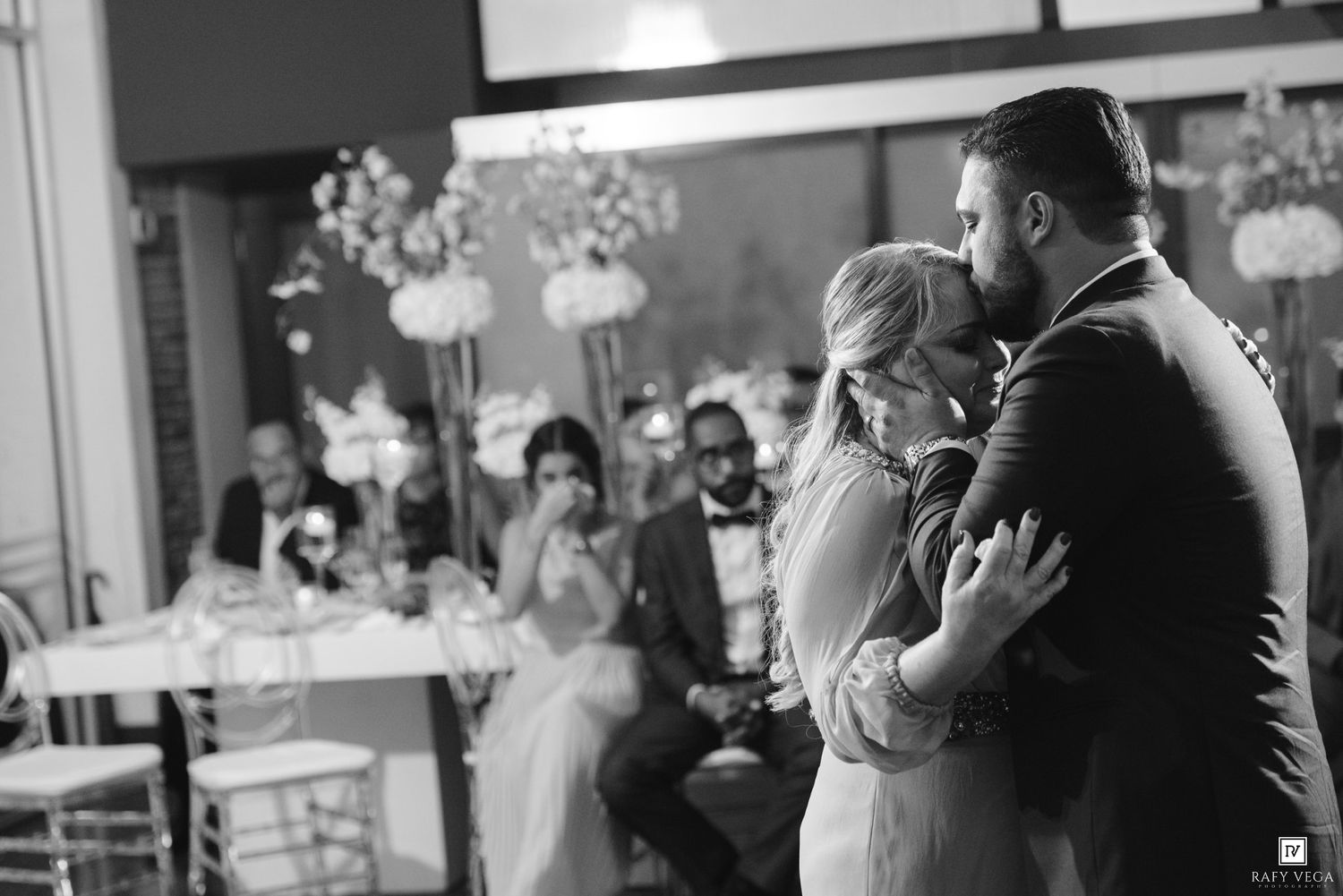 Bride and groom share an emotional first dance embrace at elegant wedding reception in black and white photo.