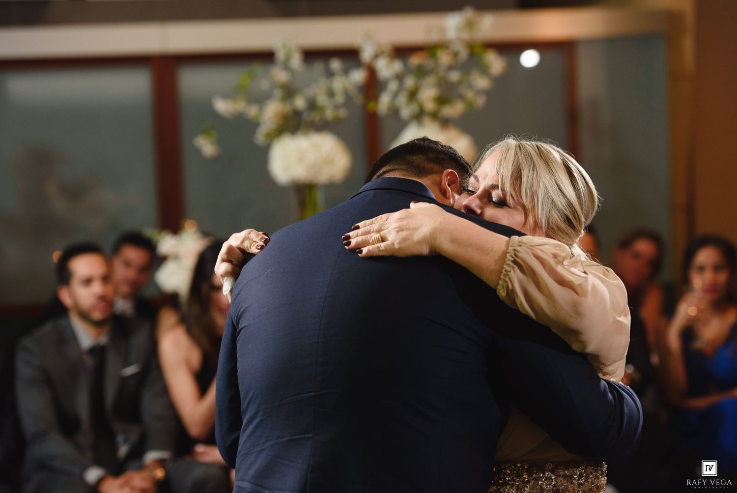 Emotional wedding moment as couple shares a heartfelt hug during ceremony while guests watch in background.