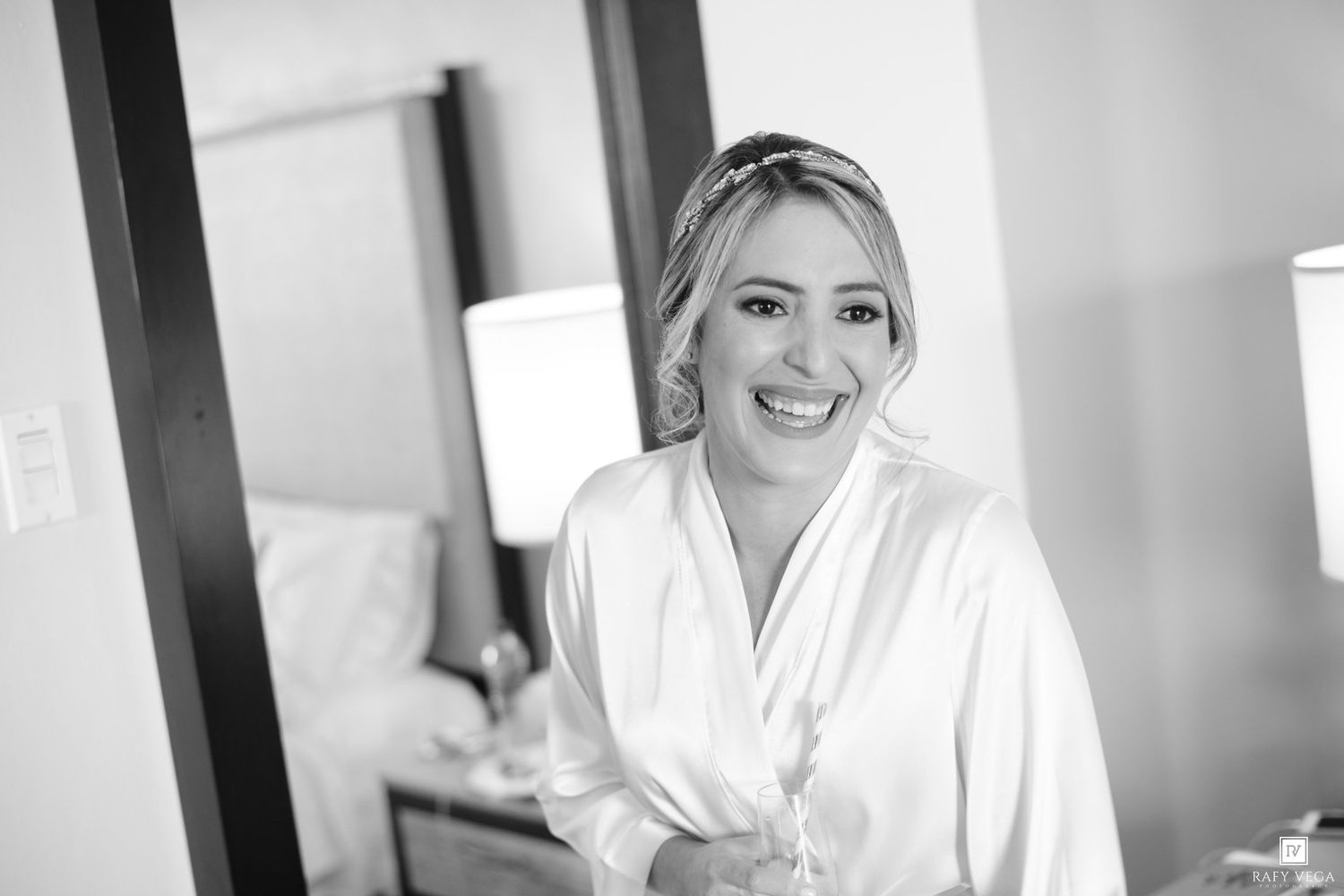 Smiling bride in white satin robe getting ready on her wedding day, black and white photo.