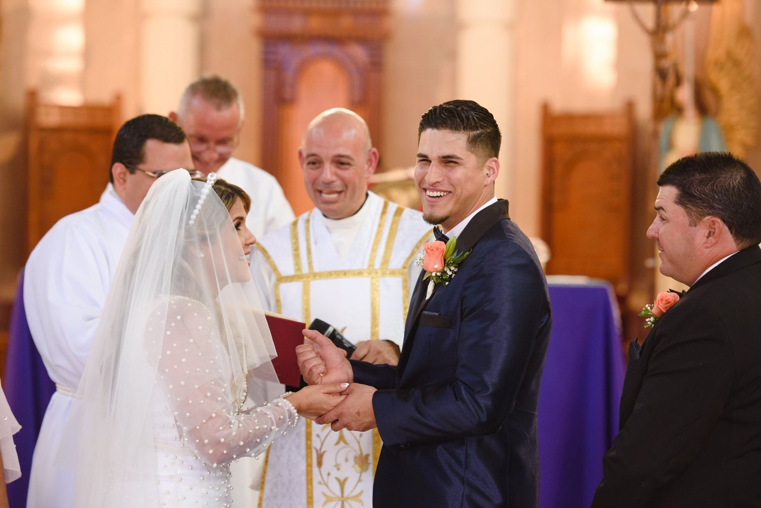 Bride and groom exchange vows at church altar with smiling priest officiating traditional wedding ceremony.