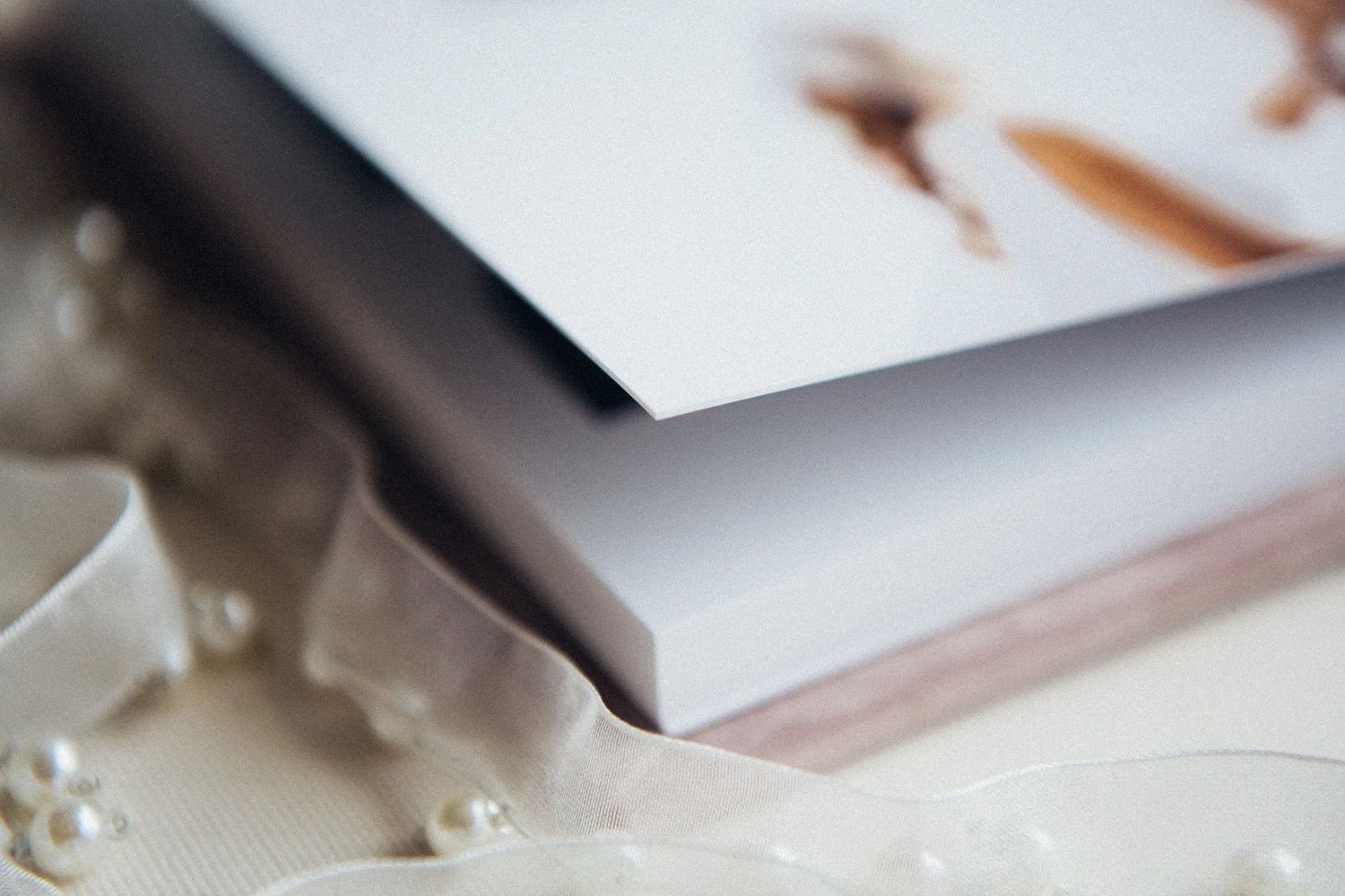 Close-up of a elegant photo album with gray cover resting on white ribbon and pearl decorations.