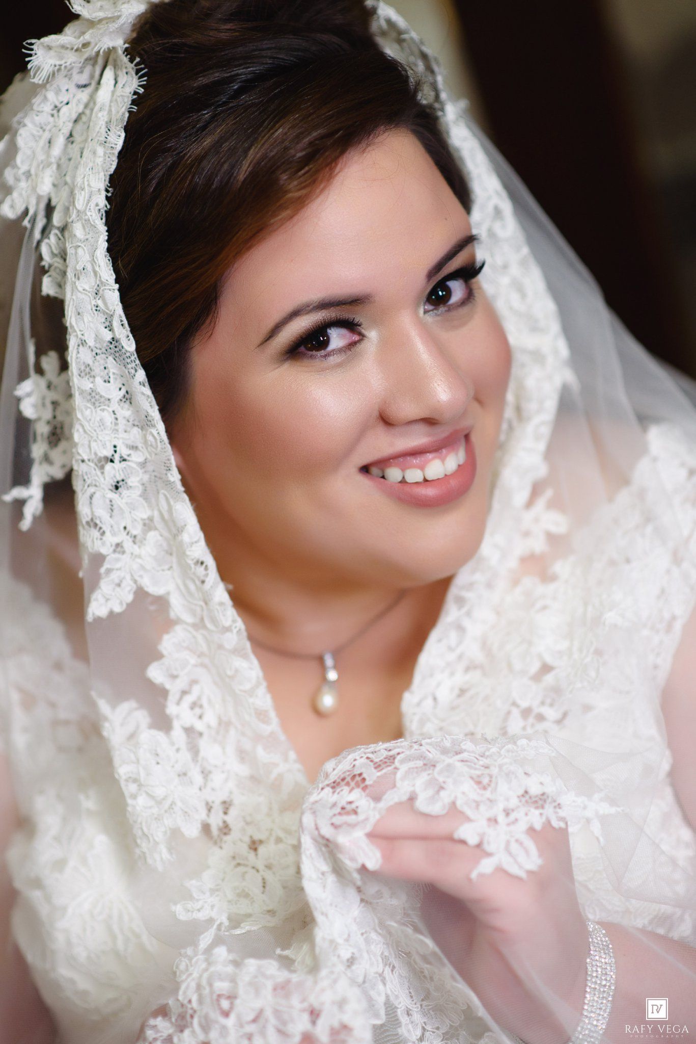 Smiling bride in white lace veil and gown with pearl necklace on her wedding day.