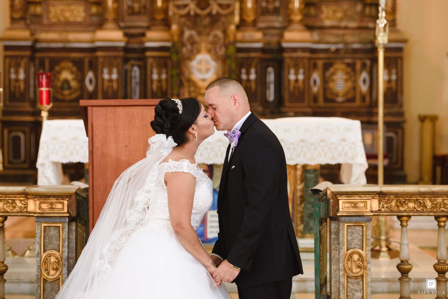 Bride and groom share a tender kiss at the altar of an ornate church during their wedding ceremony.
