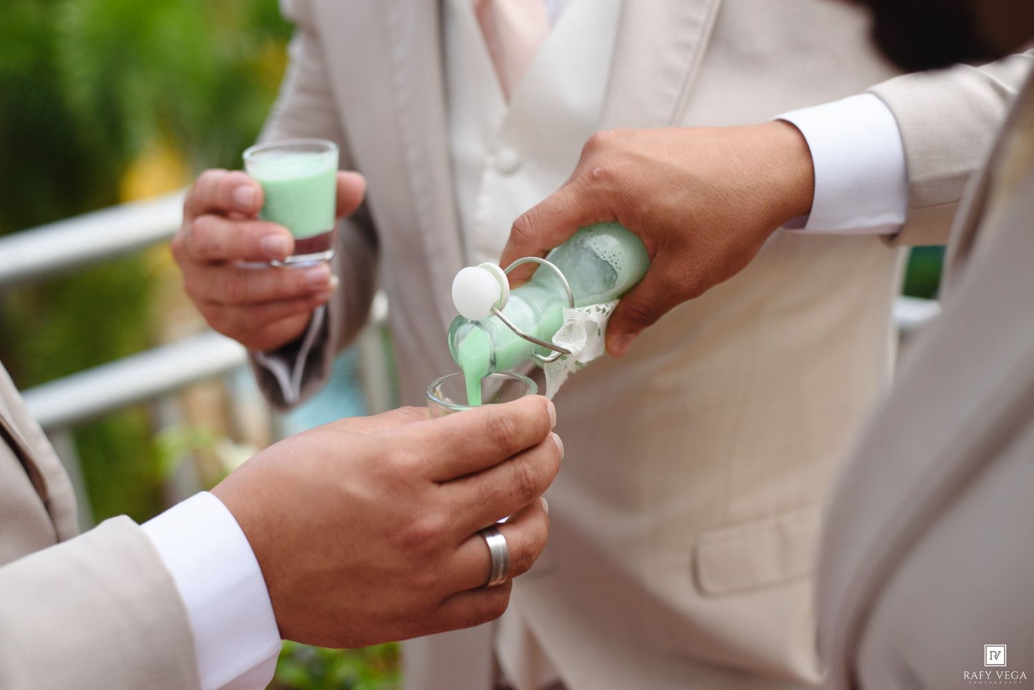 Men in suits pouring green drinks into glasses during a wedding ceremony celebration.