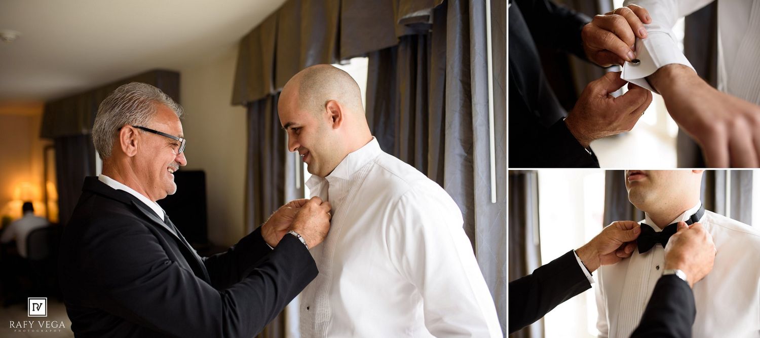 Two men in white dress shirts help a groom prepare by adjusting his collar and bow tie before his wedding ceremony.