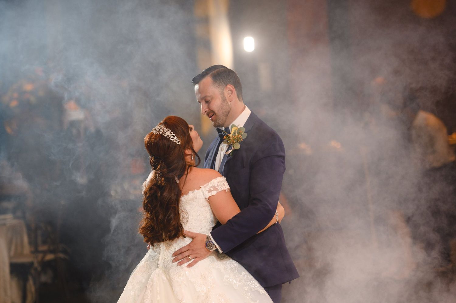 Bride and groom share their first dance surrounded by romantic fog at their elegant wedding reception.