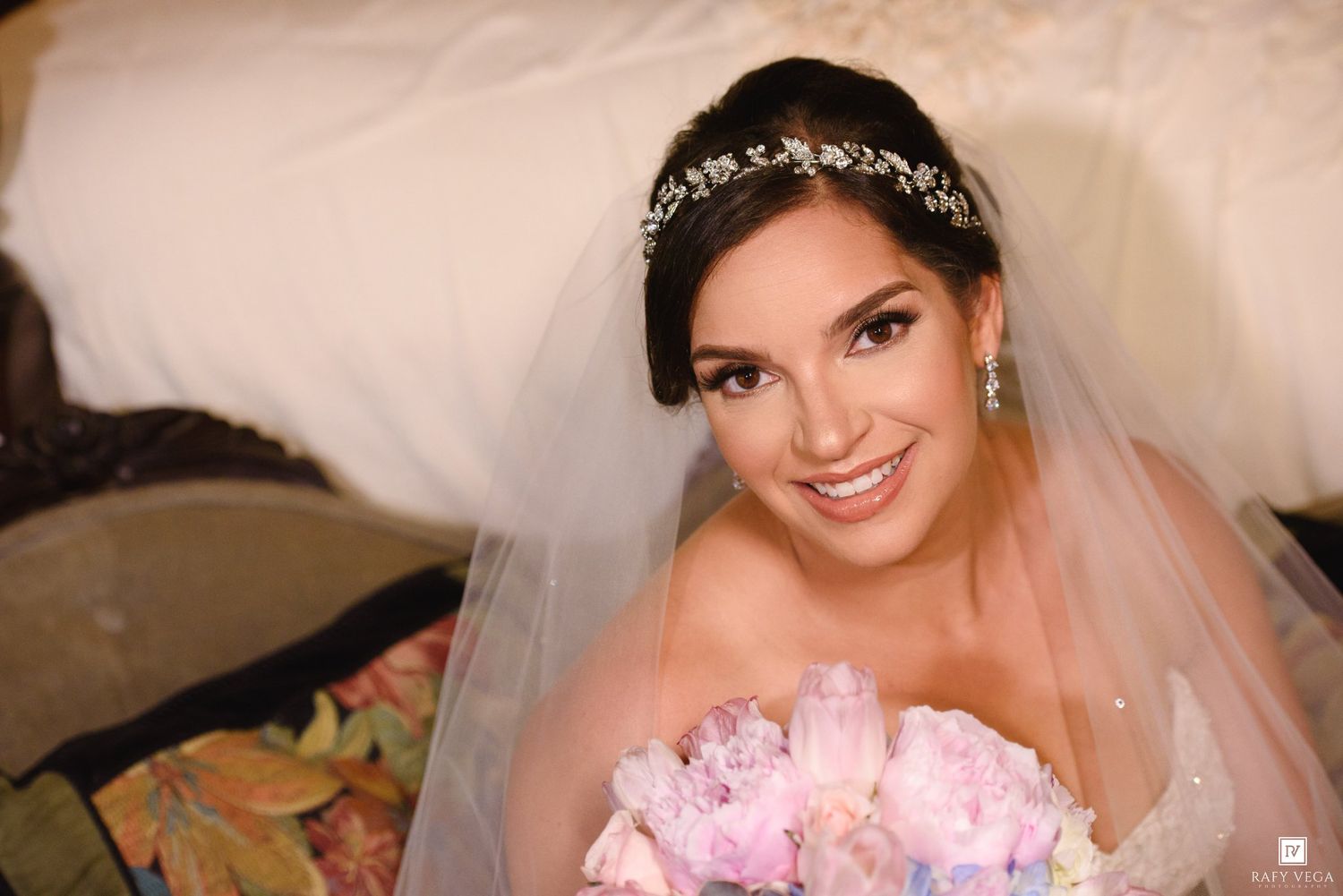 Beautiful bride smiling with floral crown headpiece and veil, holding pink bouquet in elegant bridal portrait.