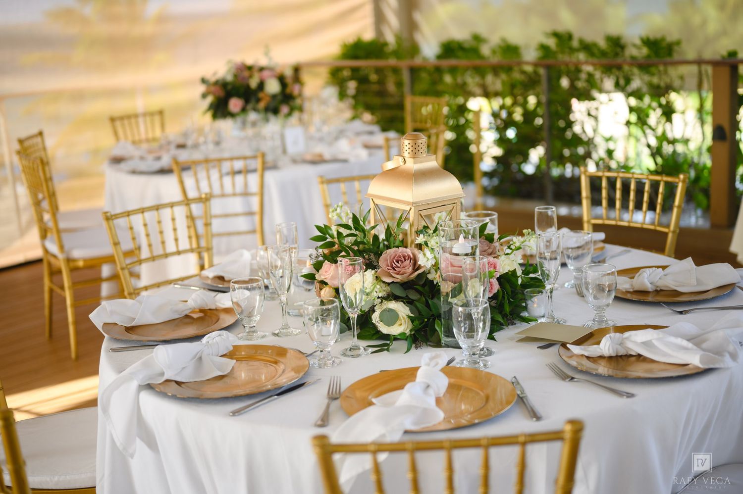 Elegant wedding reception table with gold Chiavari chairs, white linens, floral centerpiece, and crystal glassware.