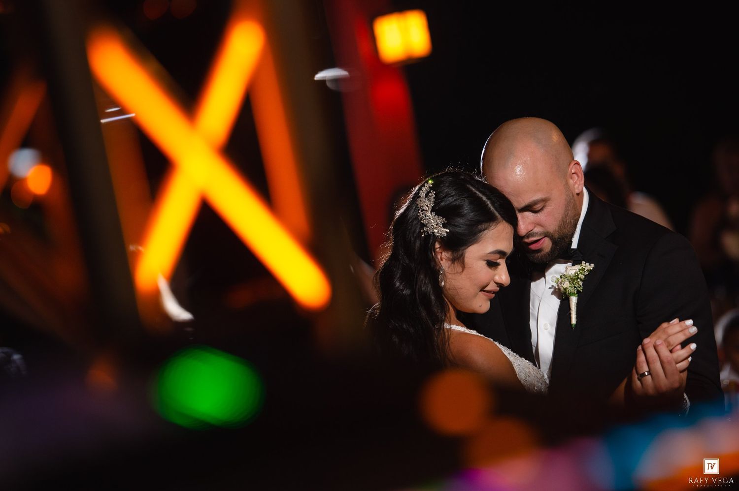 Couple sharing romantic first dance at wedding reception with warm orange X-shaped lights glowing in background.