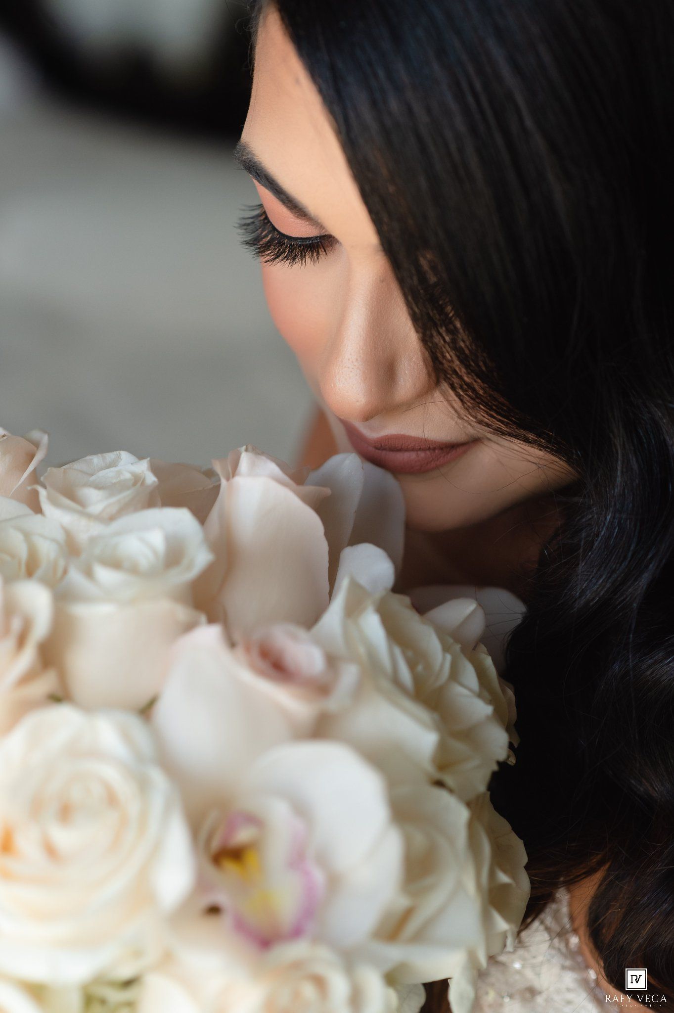 Bride with dark wavy hair smelling a lush white rose and orchid wedding bouquet.