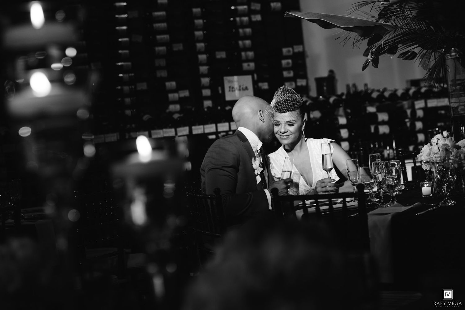 Black and white photo of a couple sharing an intimate moment at a wedding reception dinner table.